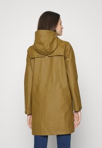 Brun vanntett regnjakke med hette, med skulderstykker, lange ermer og en avslappet passform. Glatt tekstur, designet er til knærne.