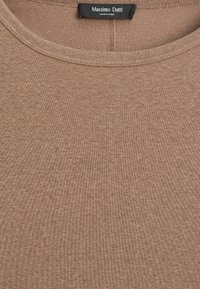 Primo piano del tessuto di un maglione marrone a girocollo con l'etichetta nera di Massimo Dutti che mostra il testo "Made in China".