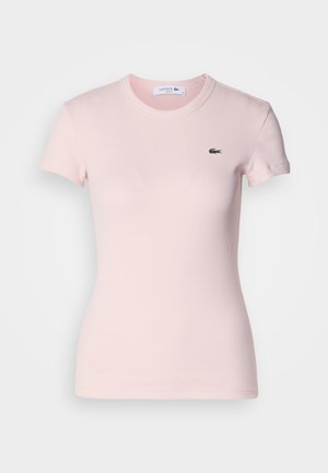 Camiseta de manga corta de color rosa claro con textura acanalada, que presenta un cuello redondo y un pequeño logo verde de Lacoste en el lado izquierdo del pecho. Textura suave.