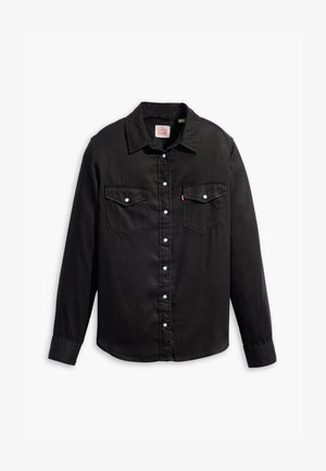 Camisa de mezclilla negra con mangas largas, cierre de botones, dos bolsillos en el pecho y un cuello clásico. Presenta una superficie texturizada y botones blancos.