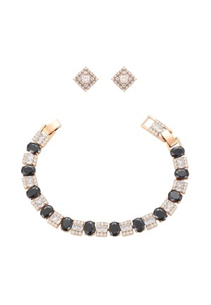 Arany karkötő váltakozó fekete ovális és fehér négyzet alakú drágakövekkel, párosítva arany négyzet alakú fülbevalókkal, fehér drágakövekkel díszítve.