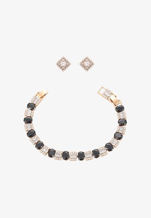 Arany karkötő váltakozó fekete ovális és fehér négyzet alakú drágakövekkel, párosítva arany négyzet alakú fülbevalókkal, fehér drágakövekkel díszítve.