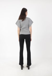 Top gris de manga corta con forma ajustada, combinado con pantalones negros de campana y tacones gruesos negros, sobre un fondo blanco.
