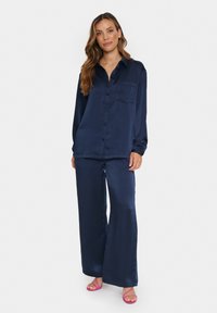 Navy satin two-piece set featuring a button-up shirt with a chest pocket and wide-leg pants. Smooth texture with a relaxed fit.