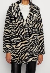 Faux fur frakke med et sort og creme zebra mønster, brede revers, to forlommer og en blød, struktureret overflade.