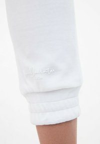 Białe, krótkie spodnie dresowe z podwinięciem, z haftowanym napisem przy mankiecie. Miękka struktura o gładkim wykończeniu.