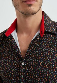 Chemise noire avec un motif paisley coloré, col rouge, doublure intérieure blanche et bouton blanc. Matériau en coton, texture lisse.