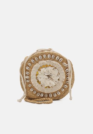 Bolso redondo de paja trenzada decorado con conchas blancas, flecos cremosos y detalles dorados con largas correas para el hombro sobre un fondo blanco.