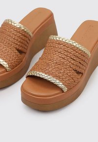 Sandalias de cuña en tono beige con textura trenzada, detalles en tono dorado y una plantilla suave y redonda. Suela de plataforma para mayor altura y comodidad.