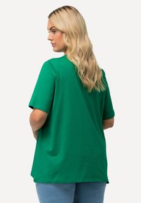 Grünes Baumwoll-T-Shirt mit kurzen Ärmeln und lockerer Passform, versehen mit einer glatten Textur und einem abgerundeten Saum, von hinten betrachtet.