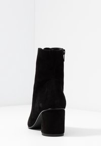 Černé semišové kotníkové boty s kulatou špičkou a blokovým podpatkem, vybavené zipovým zapínáním na vnější straně a hladkými černými akcenty.