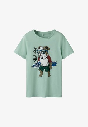 Μπλουζάκι μέντας με γραφικό ενός μπουλντόγκ που φορά γυαλιά ηλίου, λευκό και κόκκινο πουκάμισο, πράσινο σορτς και κρατά μια μπλε σανίδα σερφ.