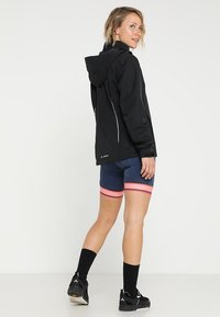 Black waterproof jacket with a hood, featuring white zipper accents. Paired with navy shorts highlighted by red striped bands.