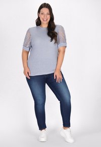 Lyseblå tekstureret strikbluse med blonder på ærmerne, parret med mørkeblå slim jeans og hvide sneakers.