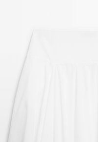 Jupe blanche taille haute avec large ceinture et plis souples, présentée sur un fond blanc uni.