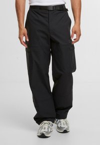 Schwarze Cargo-Hosen mit lockerer Passform, ausgestattet mit Seitentaschen, einem Gürtel und einer glatten Stofftextur. Entwickelt für Funktionalität und Komfort.