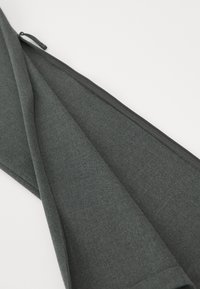 Tissu gris texturé avec un motif subtil, présentant une fermeture éclair le long du bord supérieur, plié pour montrer sa doublure intérieure.
