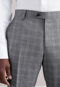 Pantalon à carreaux gris avec une texture lisse, doté d'une fermeture à un bouton et de poches latérales, associé à une chemise blanche à boutons.