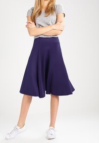 Falda A-line de color marino hecha de una tela suave, de longitud hasta la pantorrilla, con una textura lisa y un diseño fluido, combinada con una camiseta gris estampada y zapatillas blancas.