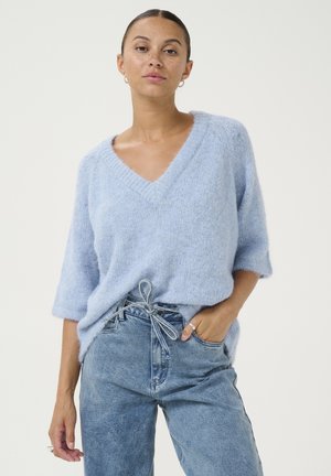 Maglione lavorato a maglia di un delicato blu chiaro, morbido e con scollo a V, maniche corte, abbinato a jeans in denim a vita alta con un dettaglio a fiocco.