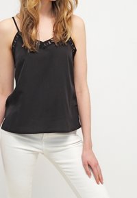 Black satin camisole with lace accents, featuring thin straps and a v-neckline, paired with white tailored pants. Smooth texture.