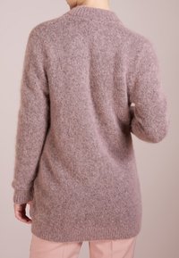 Lång, fluffig tröja i ljusrosa, med en mjuk textur, ribbade ärmslut och en avslappnad passform. Bakdelen har en subtil, rundad halsringning.