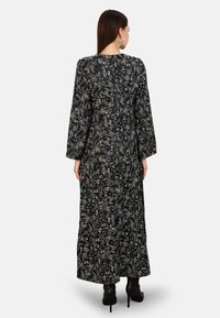 Robe maxi en tissu noir avec motif floral blanc, manches longues, encolure arrondie et design fluide, associée à des bottes à talons noires.