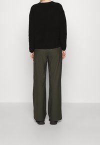 Czarny dziergany sweter z okrągłym dekoltem i opuszczonymi ramionami, zestawiony z oliwkowozielonymi szerokimi spodniami. Prosty i funkcjonalny design.
