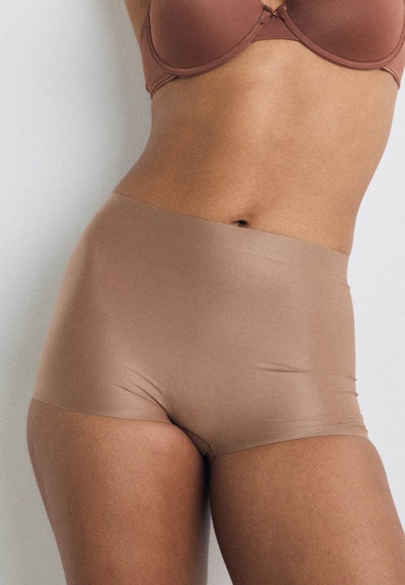 Hochgeschnittene Panty in Nude-Farbe, aus glattem, dehnbarem Stoff gefertigt. Verfügt über ein nahtloses Design ohne sichtbare Kanten.