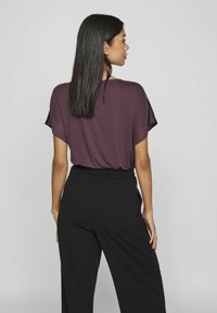 Trumpetas trumpomis rankovėmis violetinės spalvos, pagamintas iš minkštos medžiagos, derinamas su juodomis aukšto liemens kelnėmis. Paprastas dizainas, laisvas ir švelnus.