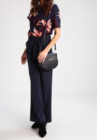Top floreale navy con maniche corte, abbinato a pantaloni a righe verticali in vita alta. Borsa a tracolla nera e stivaletti con punta.