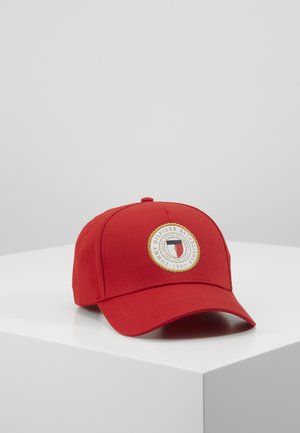 Rode honkbalpet met een ronde Tommy Hilfiger-logo patch gecentreerd aan de voorkant, geplaatst op een witte ondergrond tegen een lichtgrijze achtergrond.