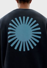 Sudadera de color azul oscuro con un gran gráfico de explosión solar en color azul claro en la parte posterior, con un centro redondo y rayos alargados que se extienden hacia afuera.