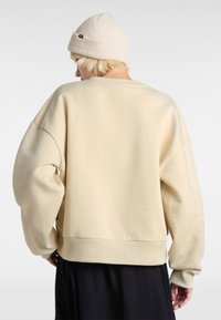 Sudadera crema con un corte relajado, hombros caídos, puños de canalé y dobladillo. Llevada con un gorro de punto beige claro.