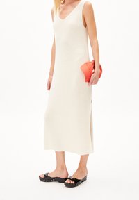 Robe en tricot côtelé crème avec un décolleté en V profond et des fentes sur les côtés, associée à des sandales à plateforme noires avec des accents argentés et une pochette rouge.