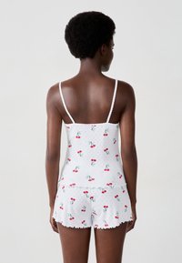 Set da pigiama bianco composto da una canotta senza maniche e pantaloni corti, decorato con una stampa di ciliegie, bordino ondulato e un tessuto morbido e leggero.