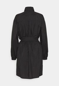 Veste légère noire avec col montant, manches longues, taille cintrée par un lien, et finition texturée. Caractérisée par une coupe droite et un léger éclat.