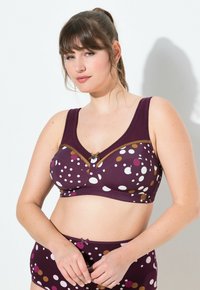 Lila gemusterter BH mit unterschiedlich großen weißen, rosa und gelben Punkten. Mit brauner Zierleiste und einem dekorativen Bogen in der Mitte.