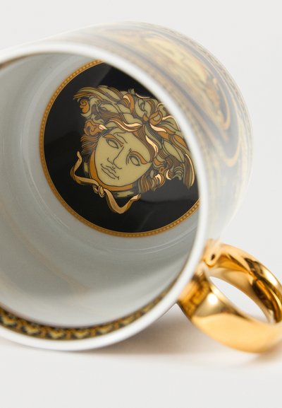 Λευκό κεραμικό φλιτζάνι με χρυσή λαβή, περίπλοκο μαύρο και χρυσό σχέδιο στο εξωτερικό και λεπτομερές χρυσό σχέδιο κεφαλής Μέδουσας στη βάση εσωτερικά.