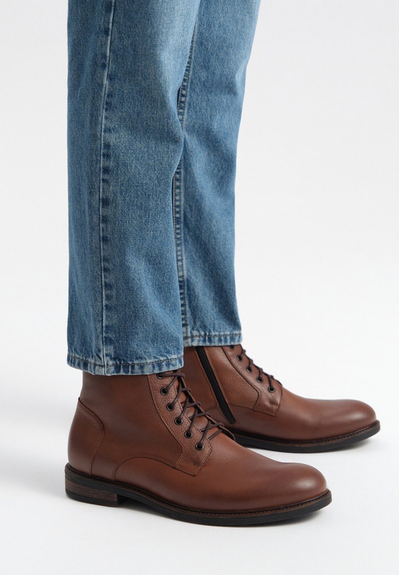 Brązowe skórzane botki za kostkę z okrągłym noskiem i wiązaniem, w połączeniu z jasnoniebieskimi dżinsami o luźnym kroju i wykończeniu na brzegach.