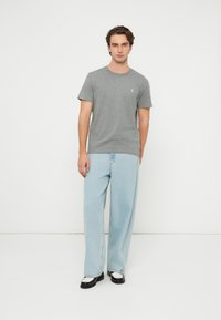 Szürke pamut rövid ujjú póló környakkal, világoskék bőszárú farmerral és fekete-fehér cipővel párosítva.