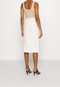 Beige tank top yhdistettynä korkeavyötäröiseen, kermaiseen midi-hameeseen, jossa on takahihna ja kaksi taskua, käytetty mustien korkokengien kanssa.