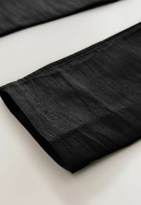 Svart, slätt tyg med en subtil glans, vikt vid fållen. Har raka kanter och en lätt textur, visas mot en ljus bakgrund.