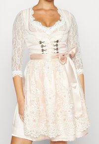 Robe en dentelle rose clair avec des manches courtes, broderie florale élaborée, décolleté en cœur et ceinture en satin nouée en nœud.