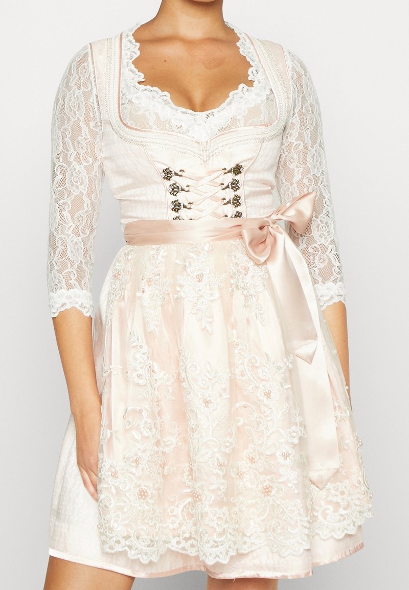 Robe en dentelle rose clair avec des manches courtes, broderie florale élaborée, décolleté en cœur et ceinture en satin nouée en nœud.