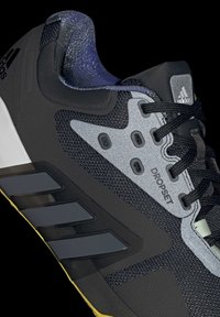 Basket noir avec des accents gris, tissu texturé, détails réfléchissants et branding à trois bandes. Comprend un col rembourré et une semelle en caoutchouc.