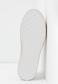 Shoe sole featuring a textured white rubber bottom with geometric patterns, transitioning to a smooth tan edge.