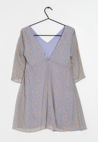 Robe bleu clair avec des motifs floraux orange et verts, décolleté en V, manches trois-quarts et silhouette évasée. Suspendue à un crochet noir.