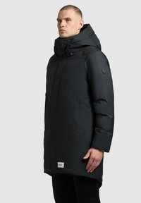 Must must coat kõrge kraega, esi lukuga ja küljetaskutega. Omab sümbolit varrukal ja sildi alumises servas.