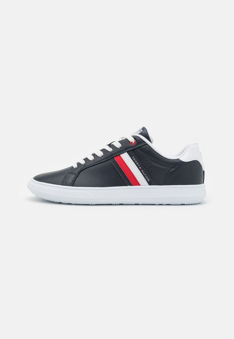 Black leather sneaker with white accents and striped red and white detail on the side. Features white sole and padded collar.